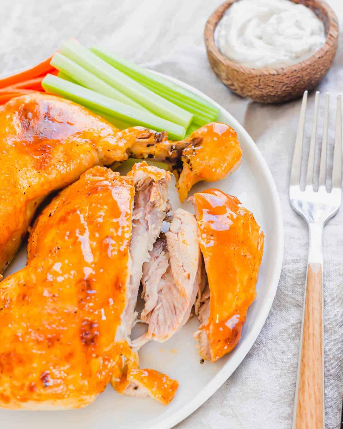 A piece of tender chicken meat cut off the bone from a chicken leg quarter on a white plate with a fork beside it.