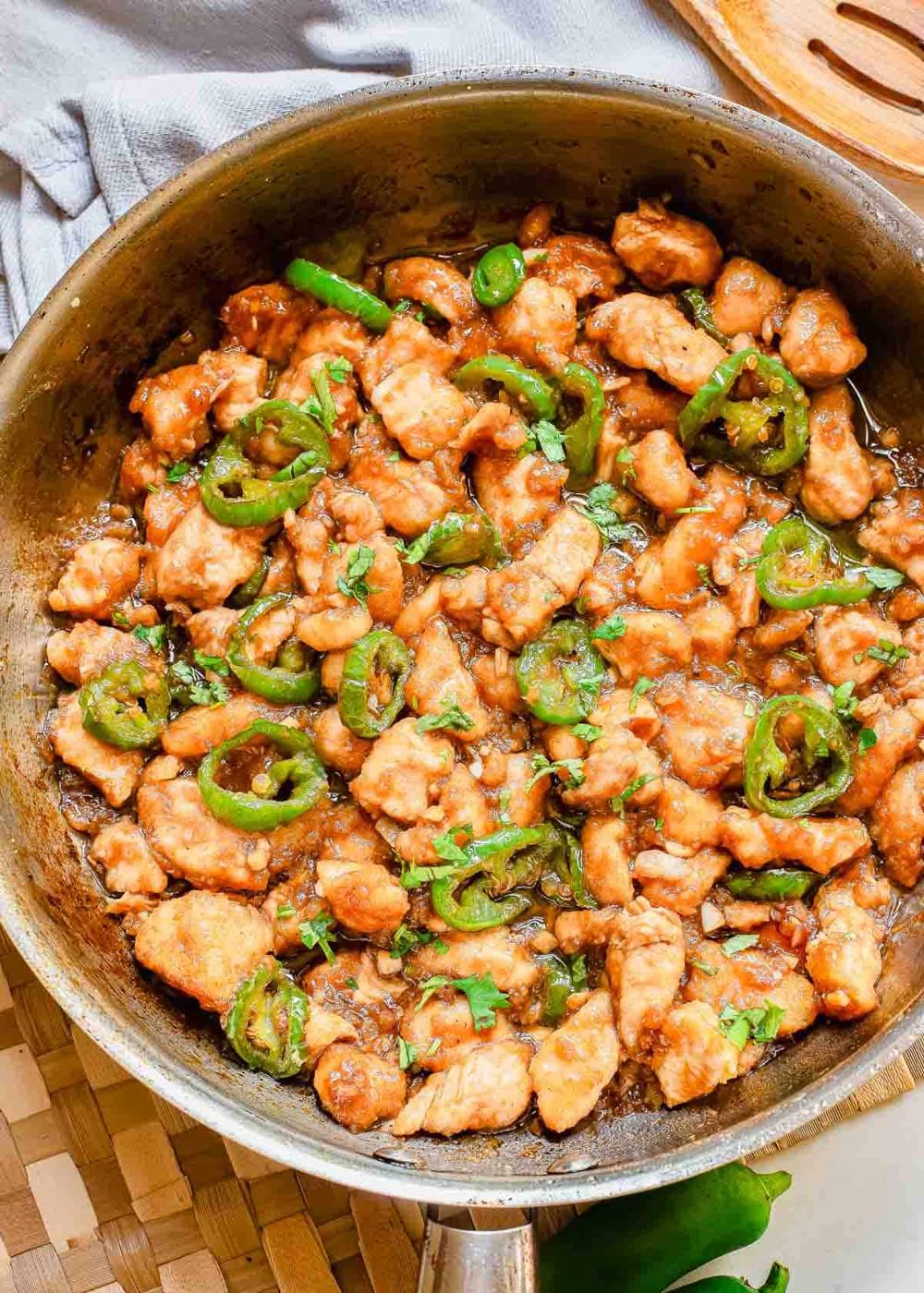 A skillet containing cooked pieces of chicken mixed with sliced green peppers and garnished with herbs.