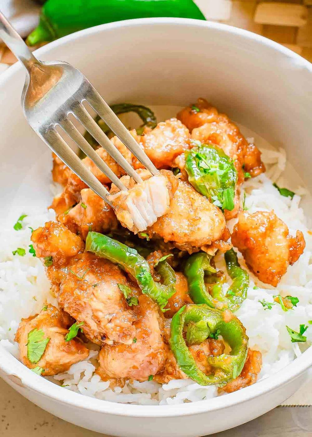 A bowl of rice topped with golden-brown cooked jalapeno chicken pieces and garnished with herbs. A fork is shown piercing a piece of chicken.