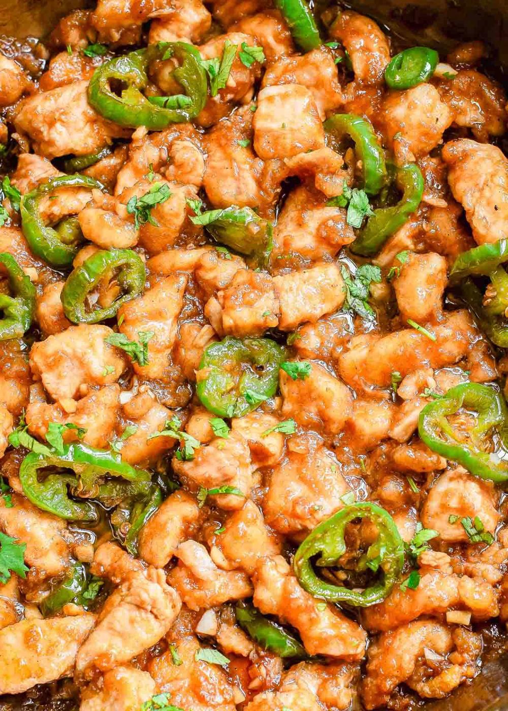 Close-up of a dish featuring pieces of cooked chicken, sliced jalapeno peppers, and a sticky sauce, garnished with fresh chopped herbs.