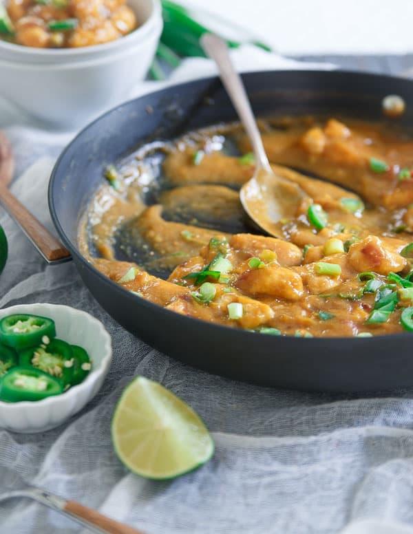 Mango chicken and sauce in a skillet need to sliced jalapeños and a lime wedge.