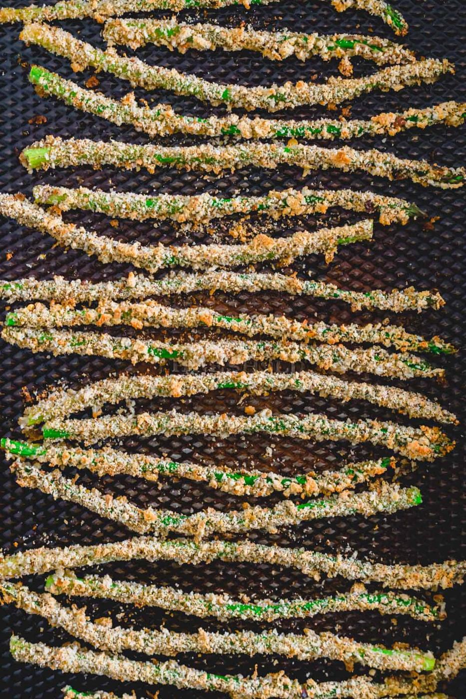 Baked asparagus fries coated in breadcrumbs on a baking sheet.