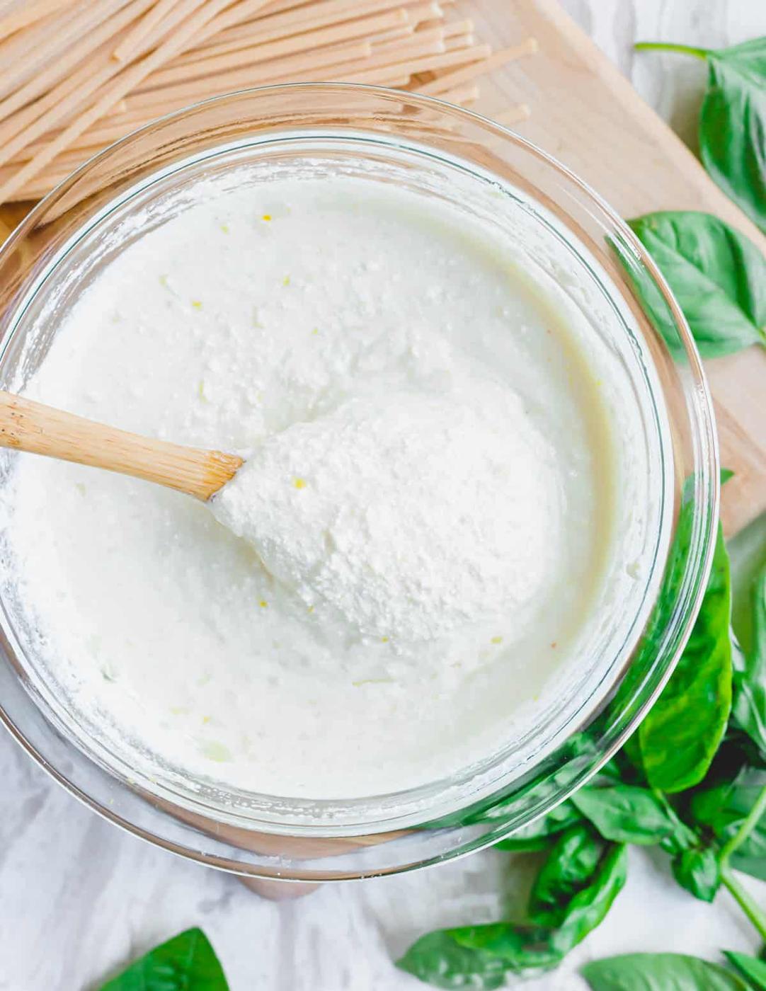 Creamy ricotta lemon garlic sauce in a glass bowl with a wooden spoon.