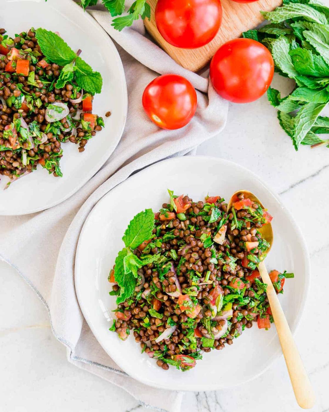 Fresh lentil tabbouleh recipe served on white plates with mint garnish and a gold serving spoon.