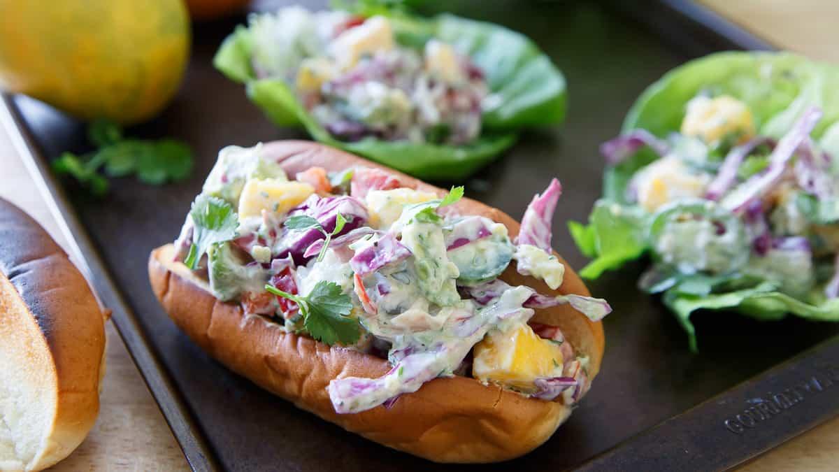 Lobster Mango Avocado Salad on a toasted bun with others on a bib of lettuce sitting on a sheet pan.