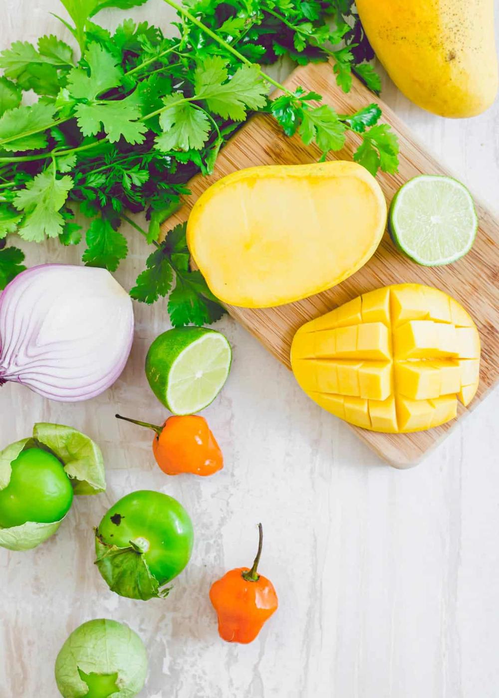 Ingredients to make mango habanero salsa including mango, lime, red onion, habanero peppers, tomatillos and cilantro.