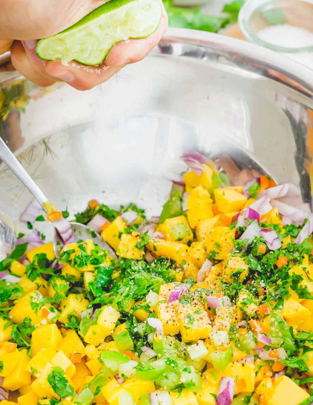 Squeezing fresh lime juice into a bowl of mango, cilantro, tomatillos, red onion and habanero peppers.