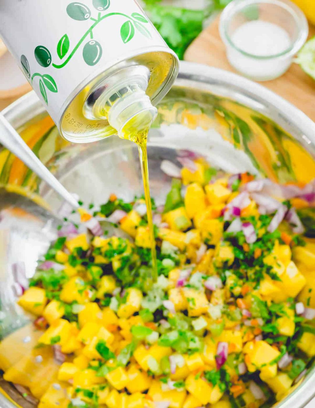 Pouring extra virgin olive oil into a bowl of mango habanero salsa.
