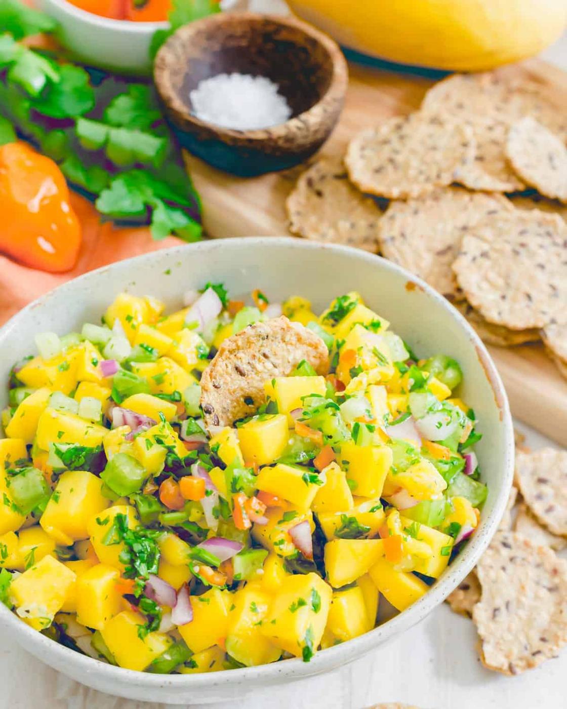 Cracker in a bowl of mango salsa with habanero peppers, cilantro, red onion, tomatillos and lime juice.