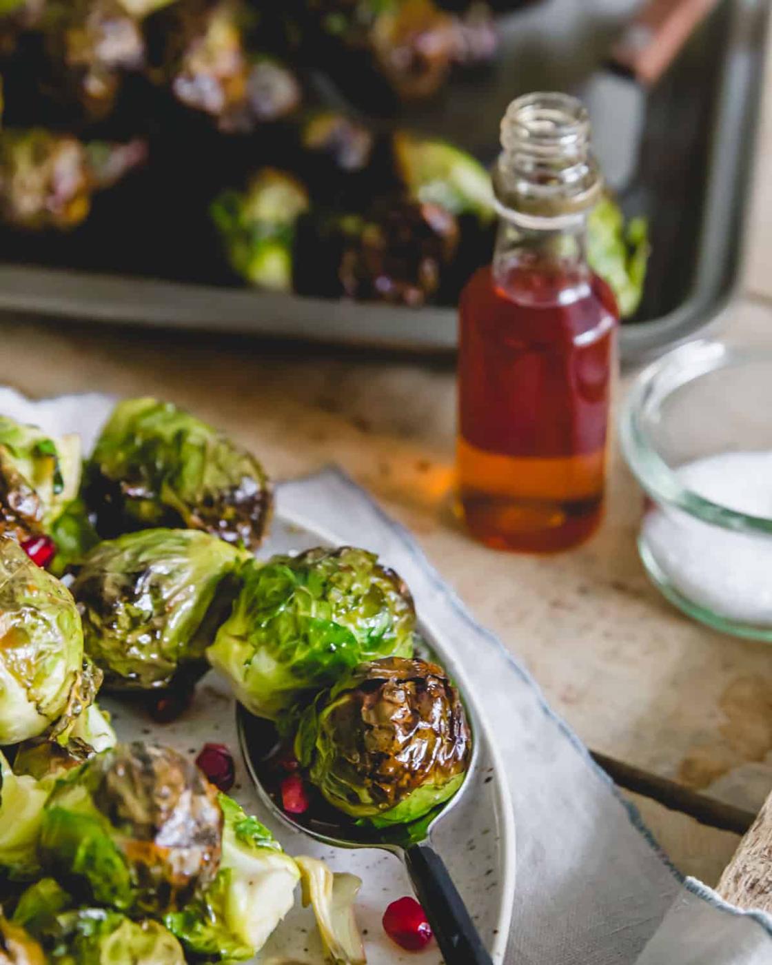 Tender maple roasted on the stalk Brussels sprouts plated and served with fresh pomegranate arils.
