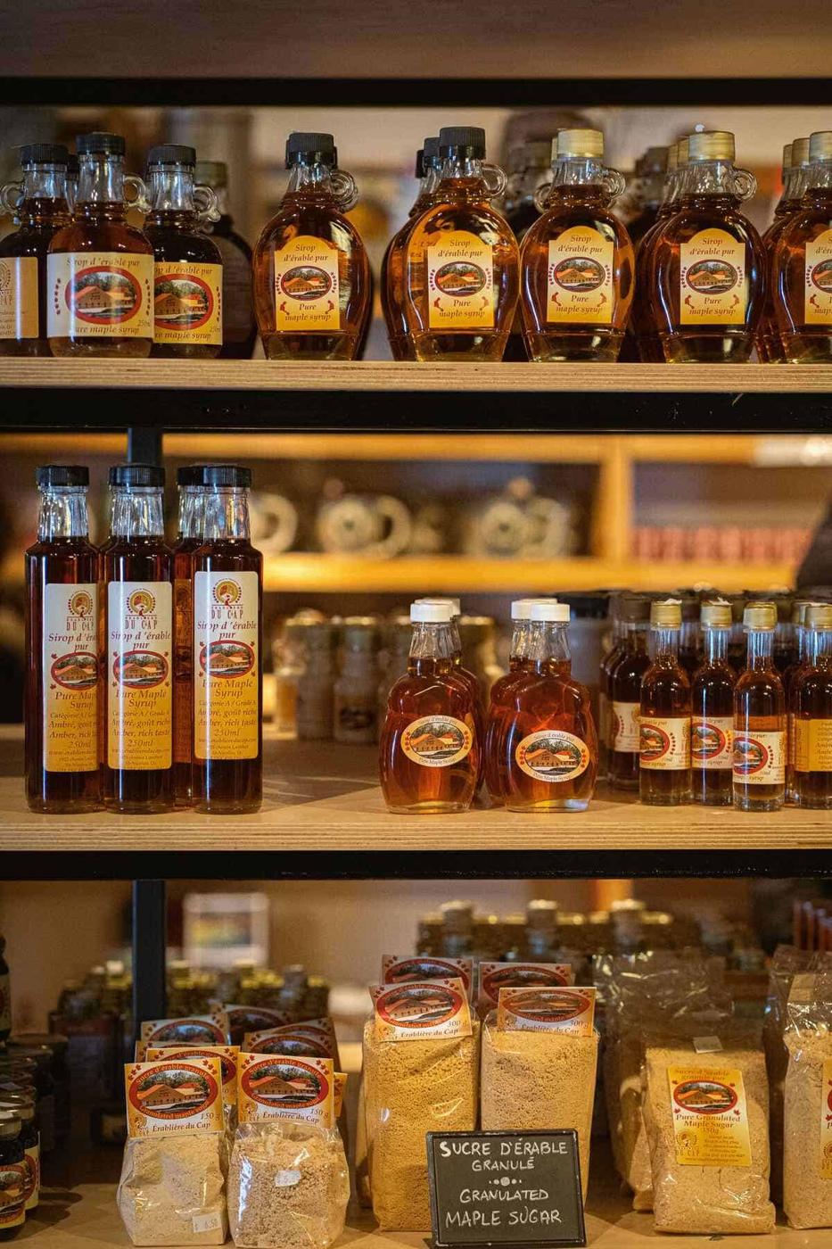 Shelves stocked with various grades of maple syrup bottles and bags of granulated maple sugar in a store.