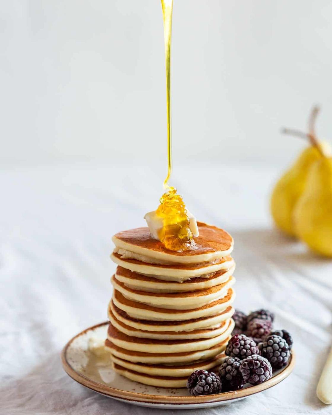A stack of pancakes with honey being poured over them.