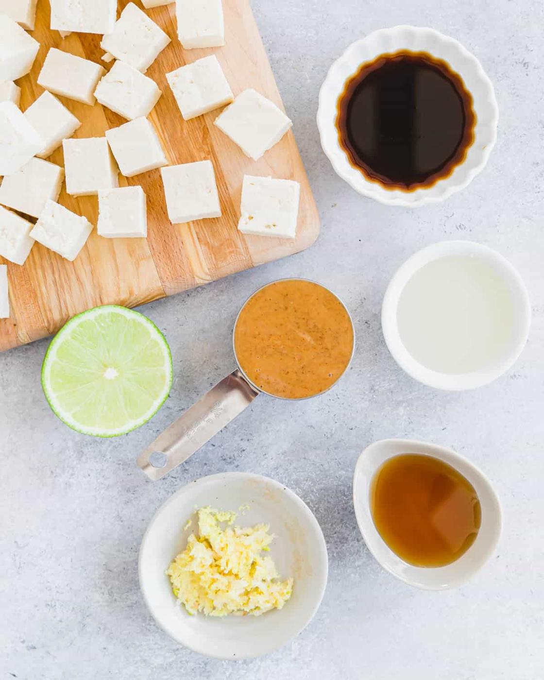 Ingredients to make creamy tofu marinade in bowls with cubed tofu on a cutting board.