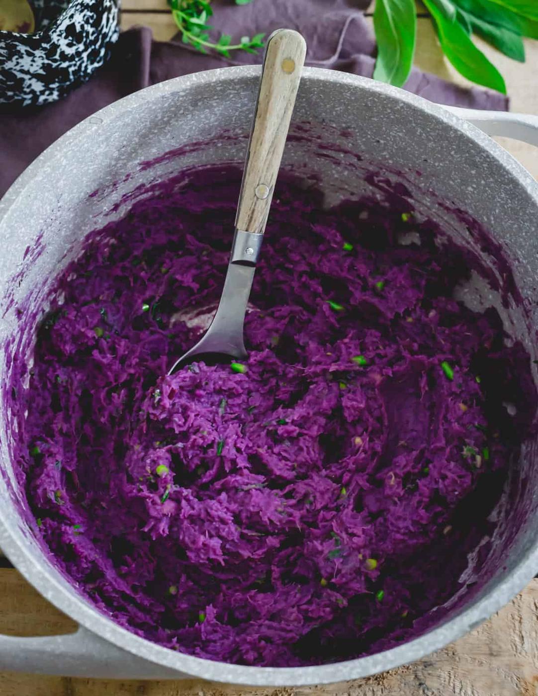 Purple sweet potatoes mashed in a pot with a spoon.