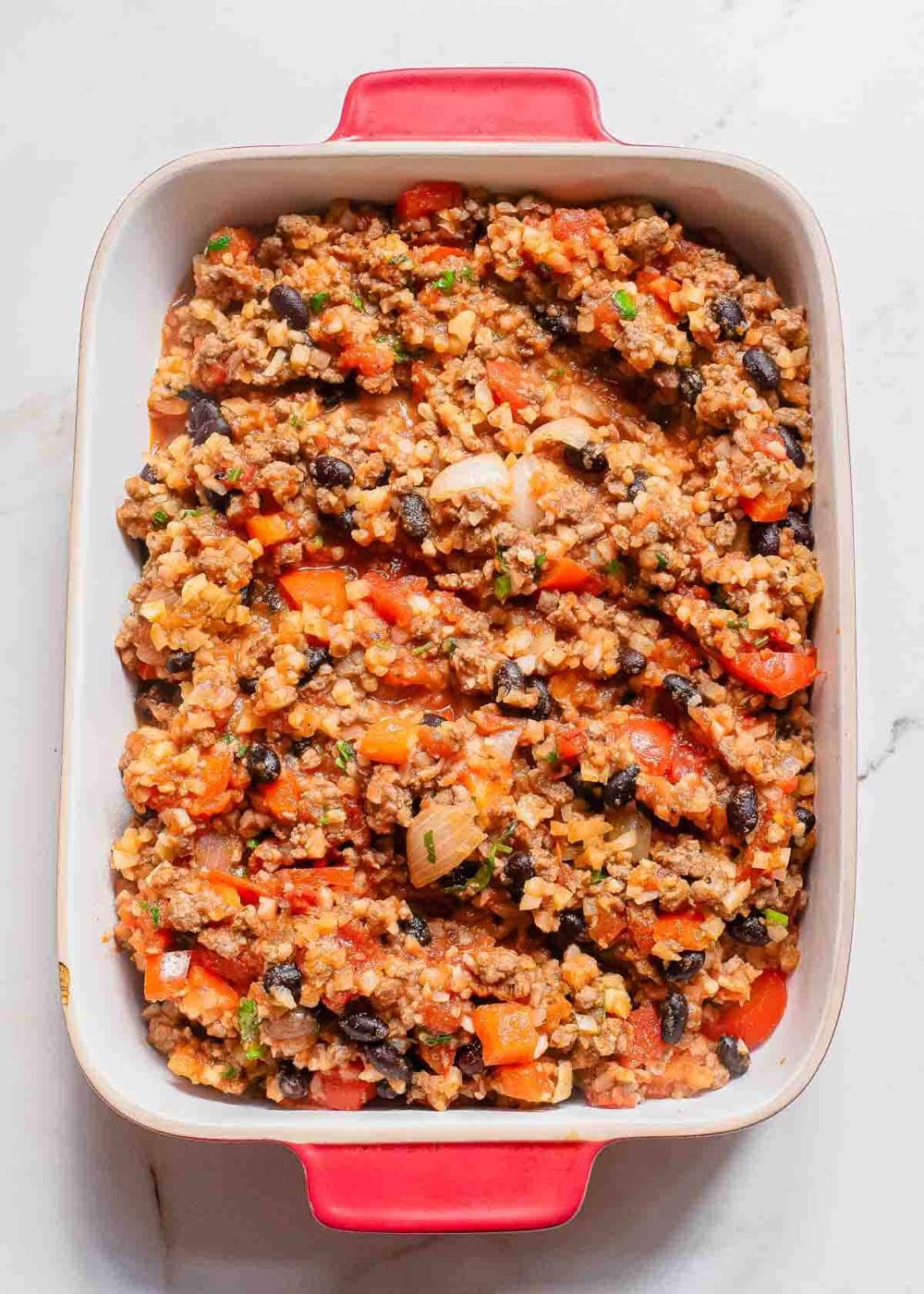 A casserole dish filled with a mixture of beef, black beans, diced tomatoes, and bell peppers.