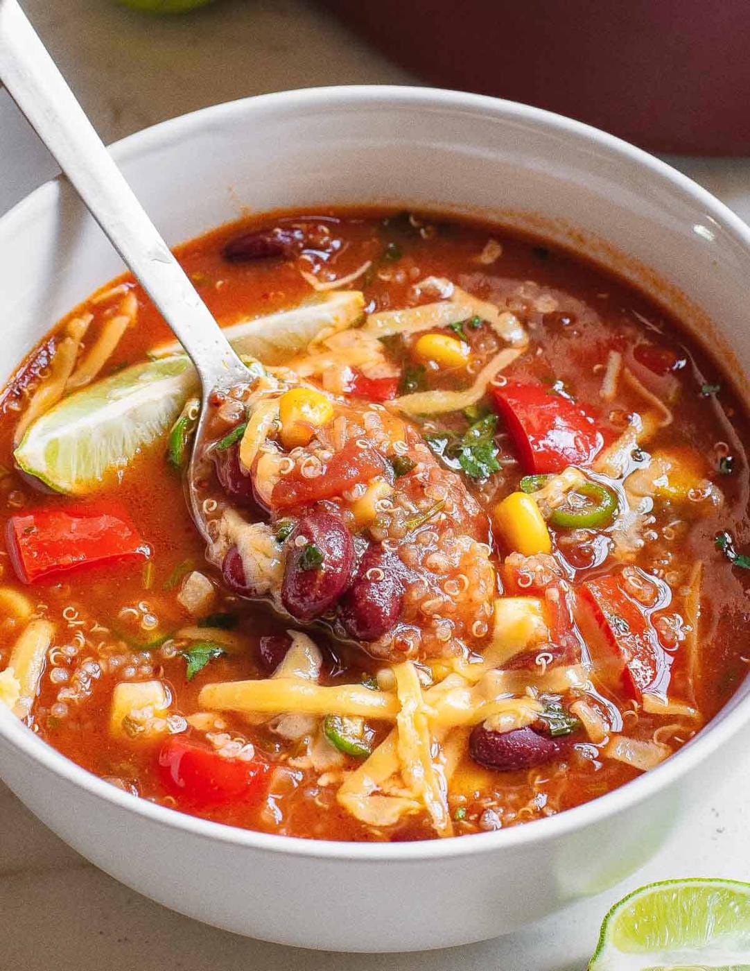 Mexican vegetable soup with beans and quinoa in a white bowl with a spoon.