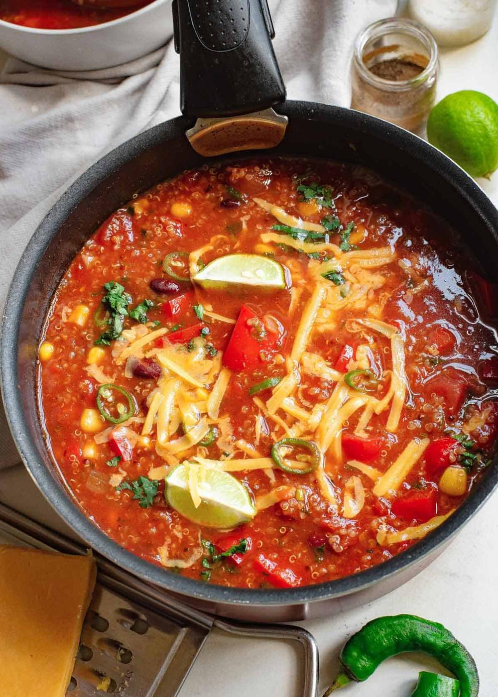 Mexican vegetable quinoa soup garnished with cheddar cheese and lime wedges in a pot.
