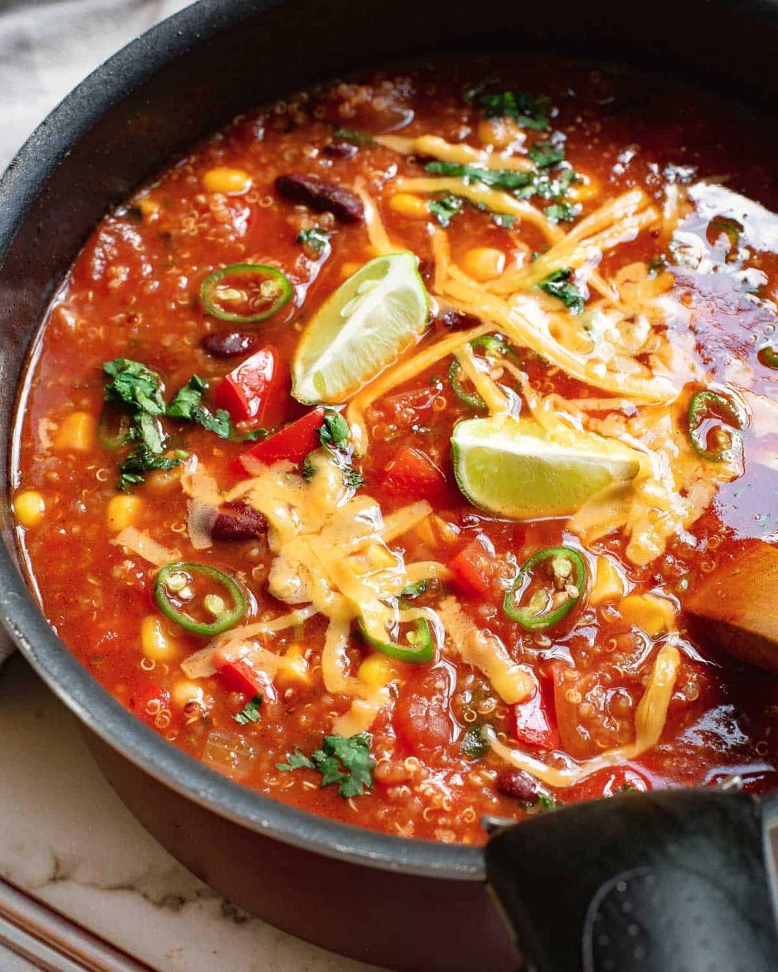 Healthy Mexican soup with vegetables in a pot garnished with lime, cilantro and cheddar cheese.