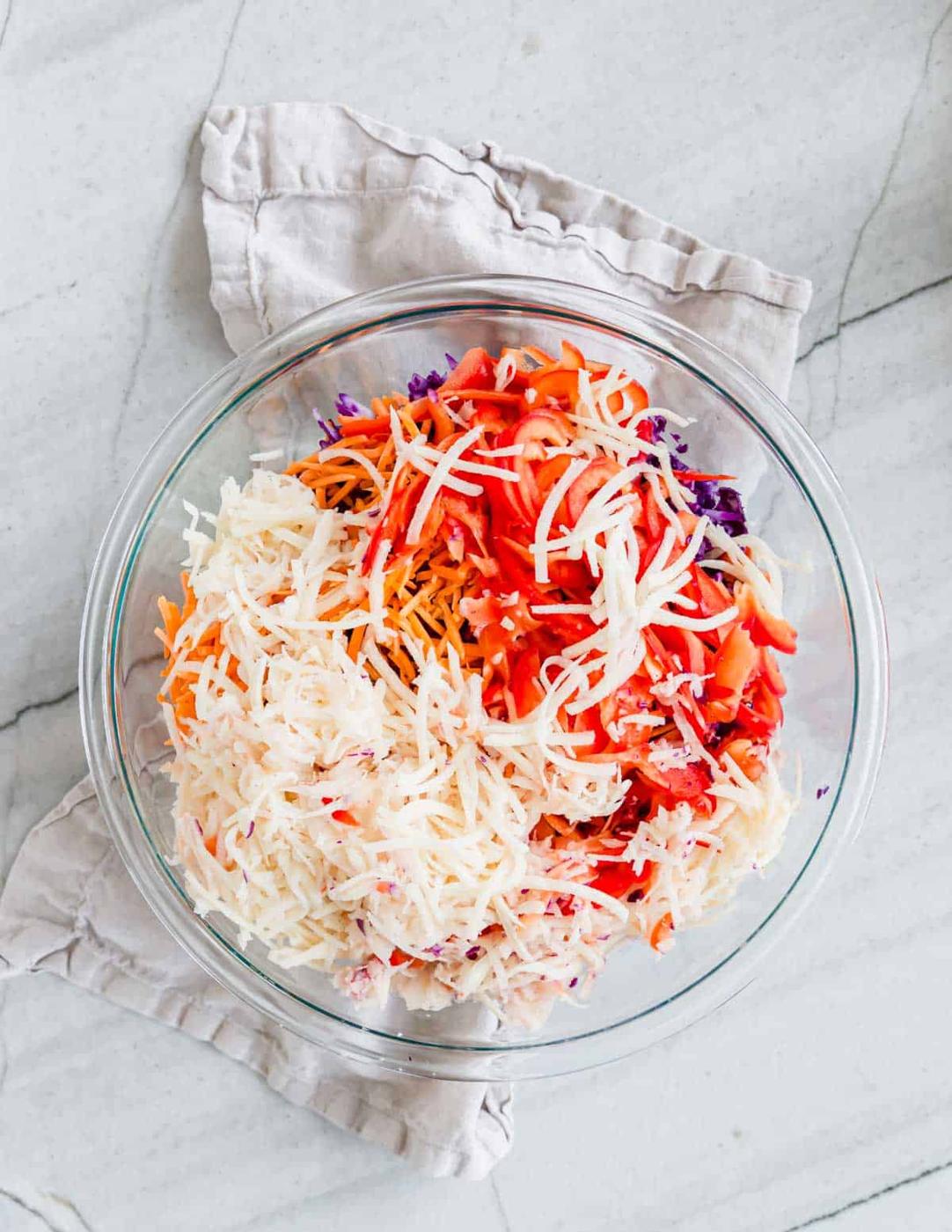 Ingredients for Irish coleslaw in a large glass bowl on a beige kitchen towel.