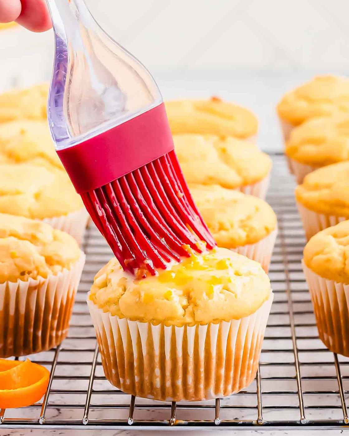 Brushing orange glaze onto muffins on a cooling rack.
