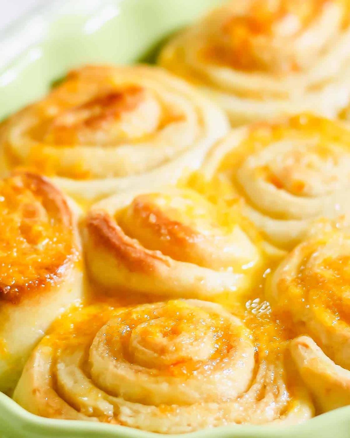 Close-up image of freshly baked orange sweet rolls with a golden-brown crust in a green baking dish.