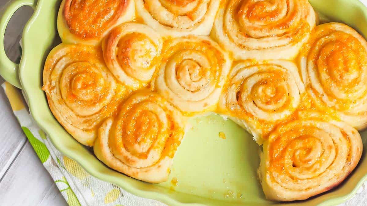 A baking dish filled with multiple orange rolls arranged in a circular pattern. One roll is missing, revealing the base of the dish.