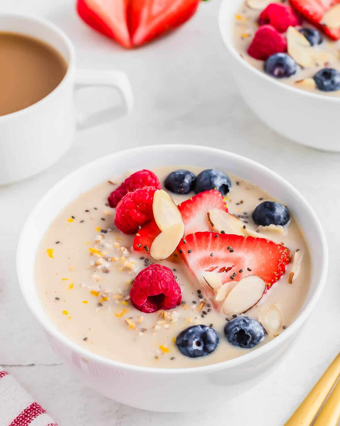 A breakfast scene containing coffee, a bowl of overnight steel cut oats with orange zest and fresh berries.