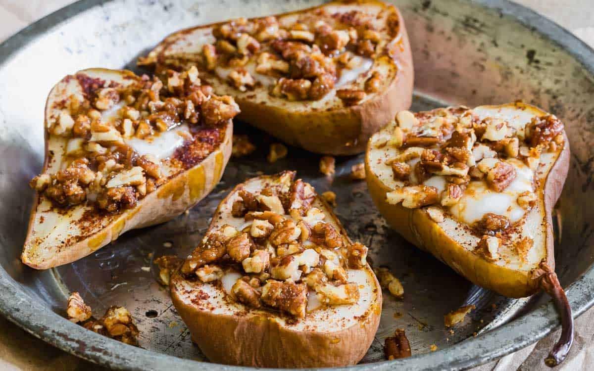 Four pear halves in a round baking dish, topped with chopped nuts and a drizzle of glaze or syrup, lightly dusted with cinnamon, and baked until golden brown.