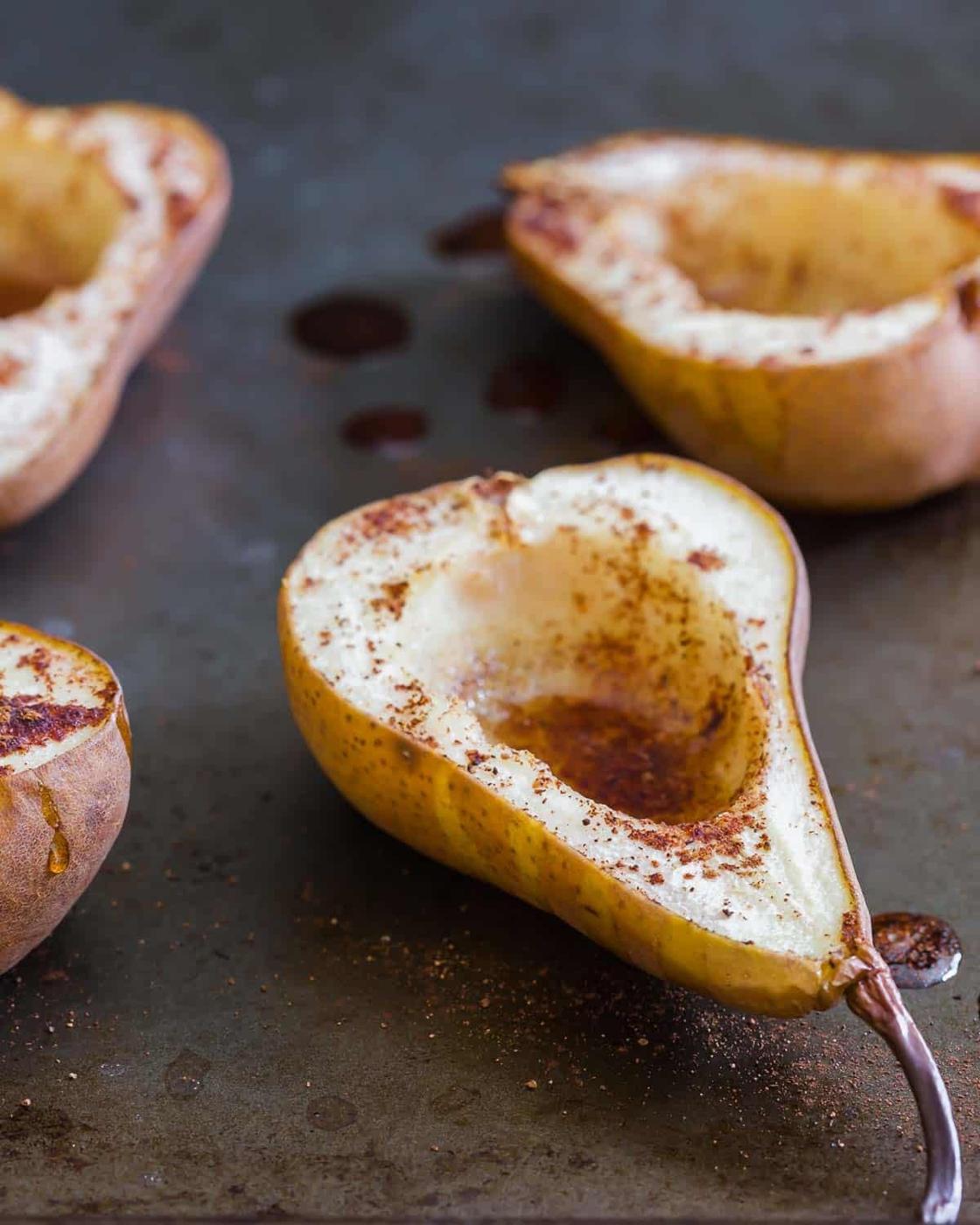 Close-up of halved pears with the centers scooped out, sprinkled with cinnamon, and placed on a baking sheet, ready to be baked.