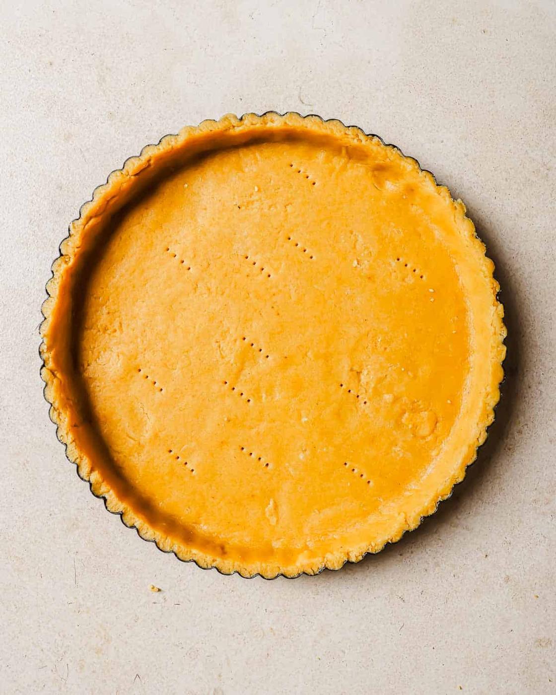Par baked tart crust in a metal pie dish on a light beige surface.
