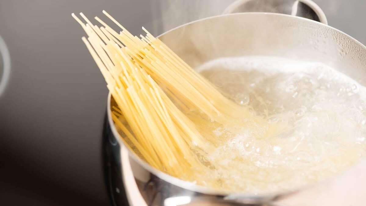 A bundle of spaghetti is boiling in a pot of water on a stovetop.