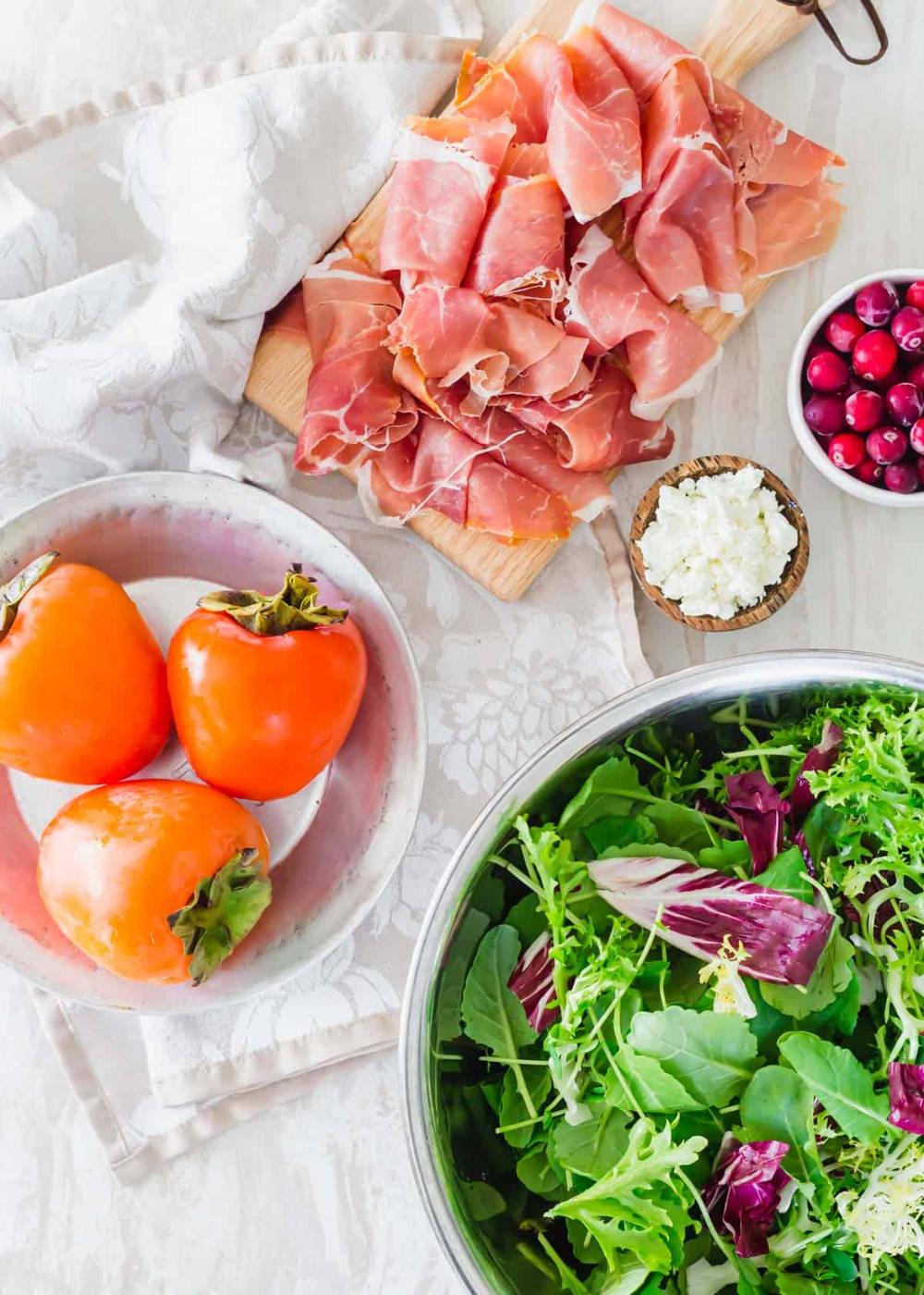 Ingredients to make persimmon salad including Hachiya persimmons, prosciutto, cranberries, goat cheese and greens.