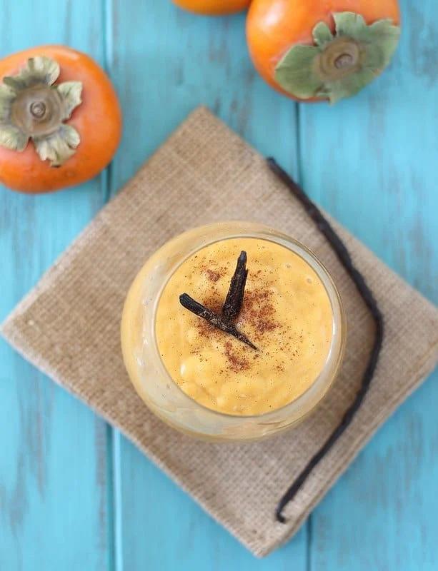 Top view of a vanilla bean persimmon smoothie garnished with cinnamon next to whole persimmons.
