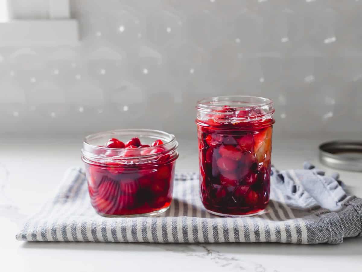 Cranberries cooling in glass jars on countertop with pickling brine.