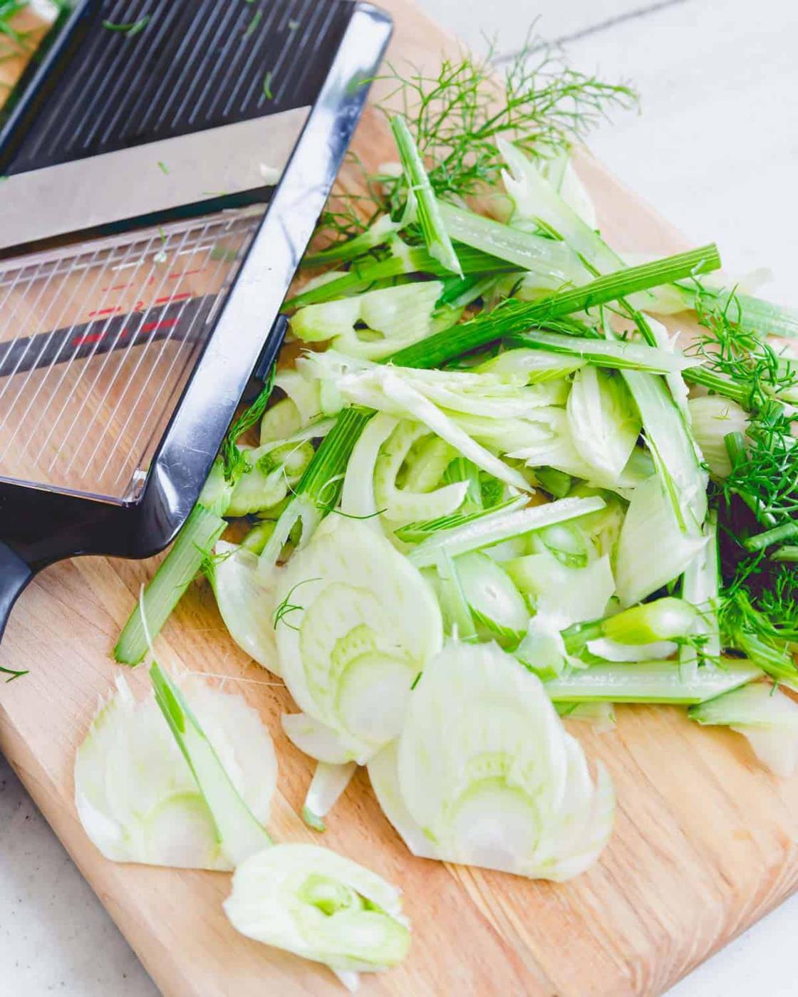 Sliced fennel on a cutting board with a mandoline slicer.
