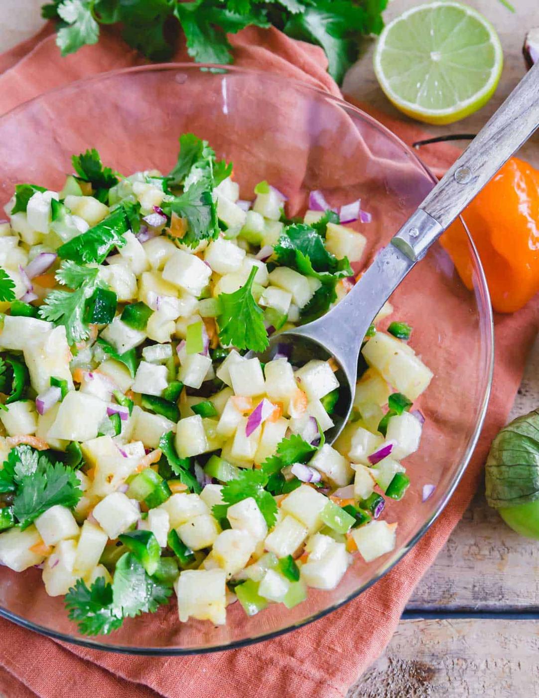 Mixing a pineapple habanero salsa recipe in a glass bowl with a metal spoon.