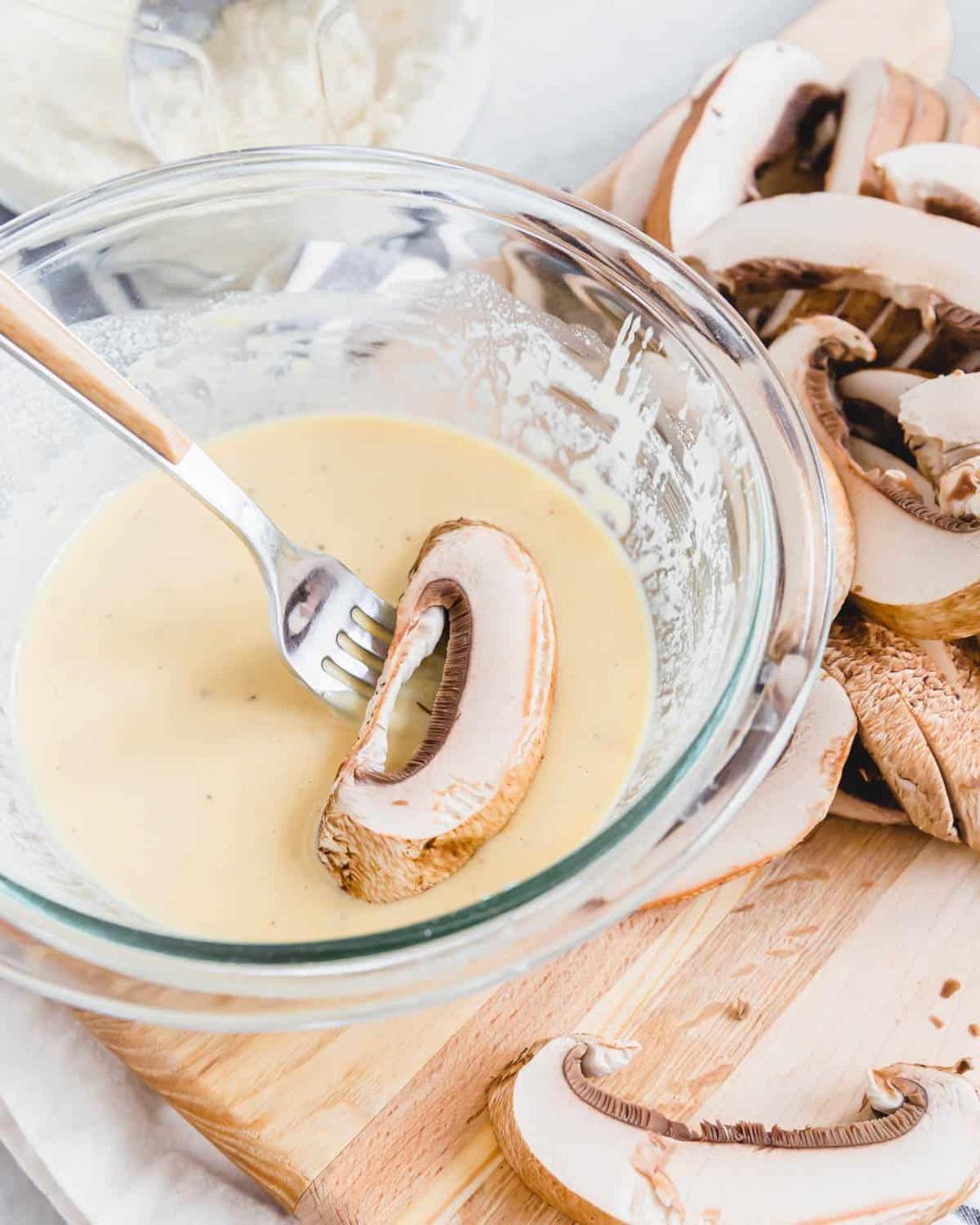Dipping a portobello mushroom slice into batter with a fork.