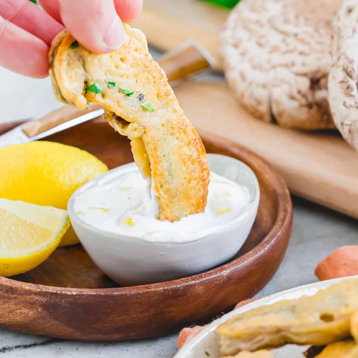 Dipping a fried portobello mushroom into a lemon yogurt dip.
