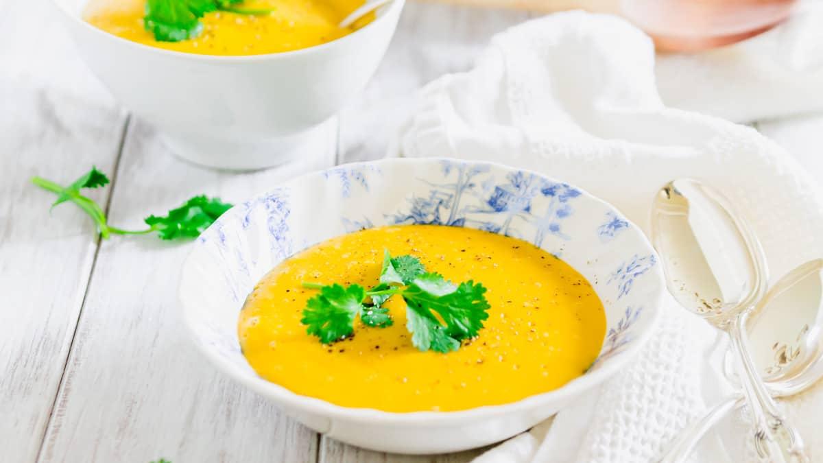 Creamy potato pumpkin soup in a bowl with parsley leaves and cracked black pepper.