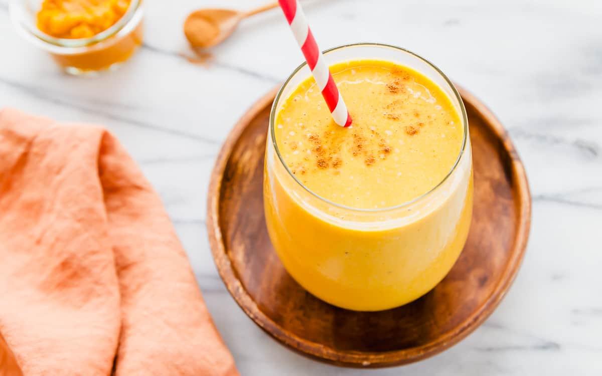 Pumpkin banana smoothie recipe in a glass with cinnamon and a red striped straw.