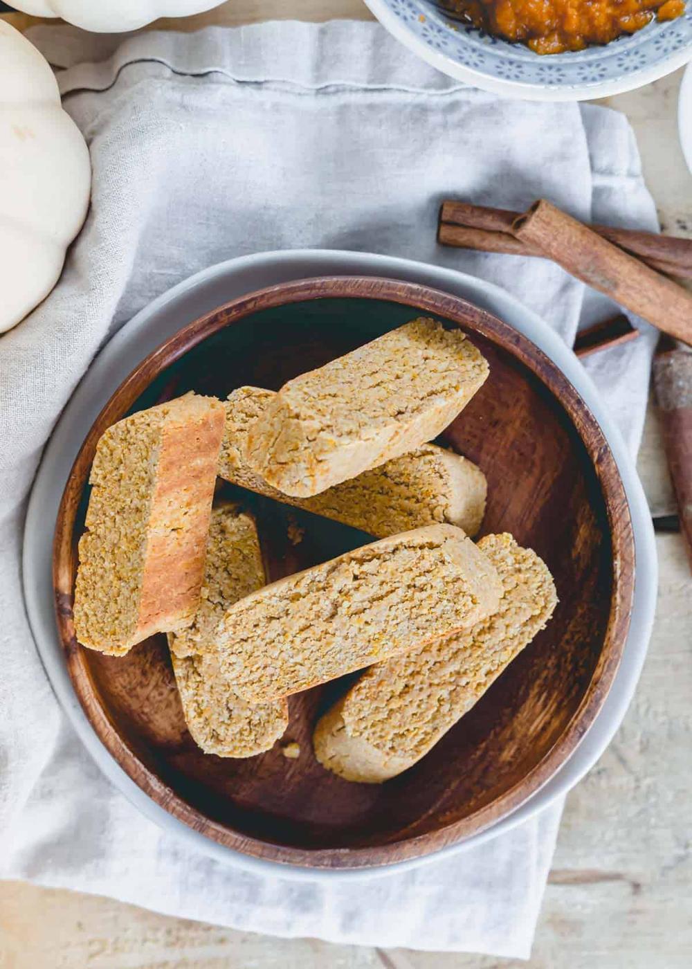 Gluten-free, vegan pumpkin spice biscotti piled on a wooden plate with a neutral cloth napkin beneath it.