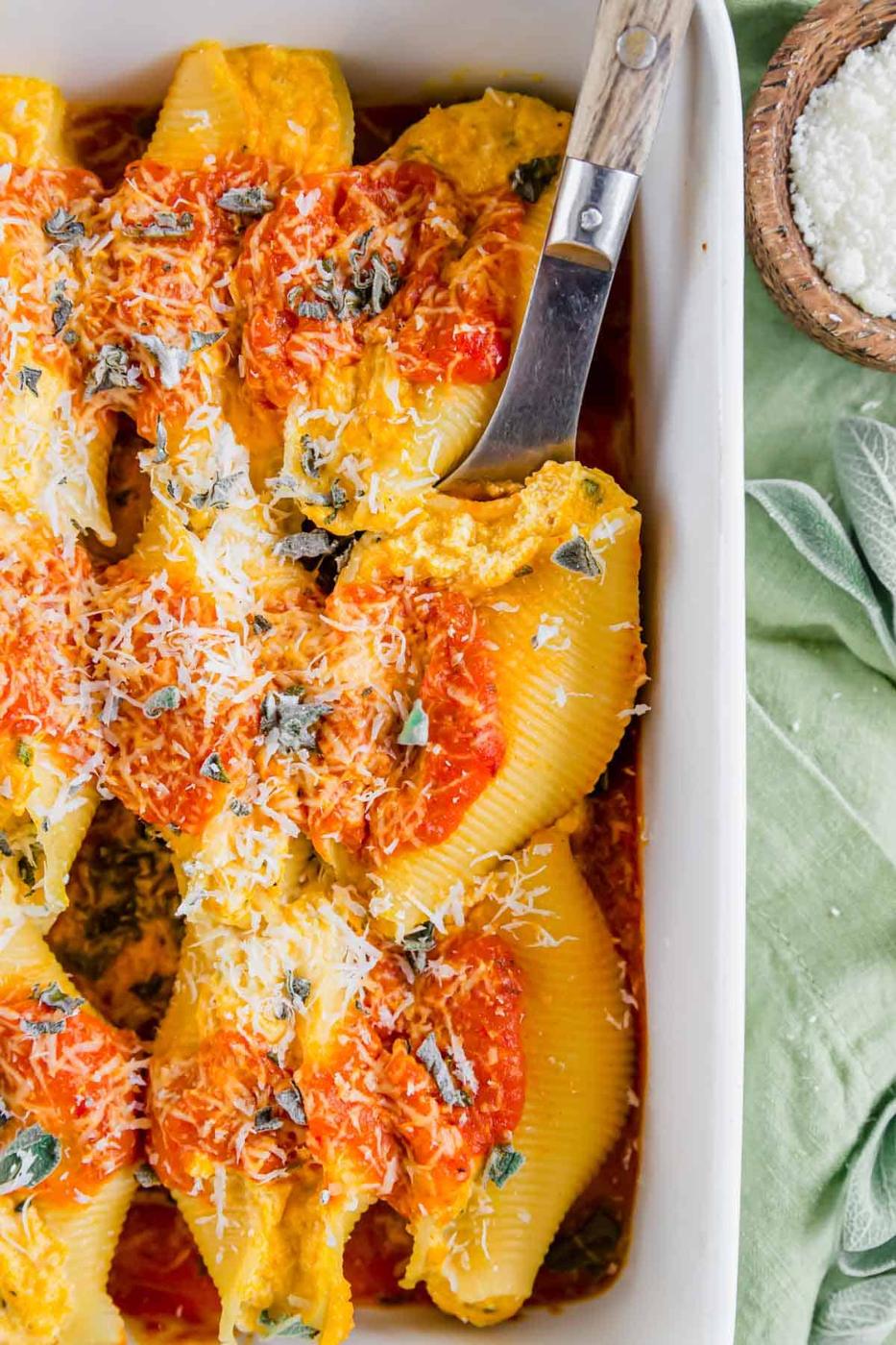 A serving spoon in a baking dish with pasta shells stuffed with pumpkin and ricotta.