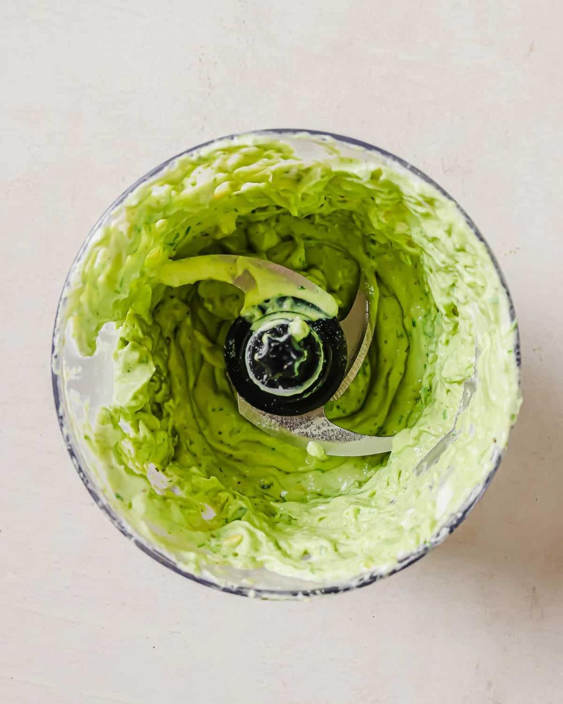 Overhead view of a blender container with a creamy avocado sauce and blades in the center.