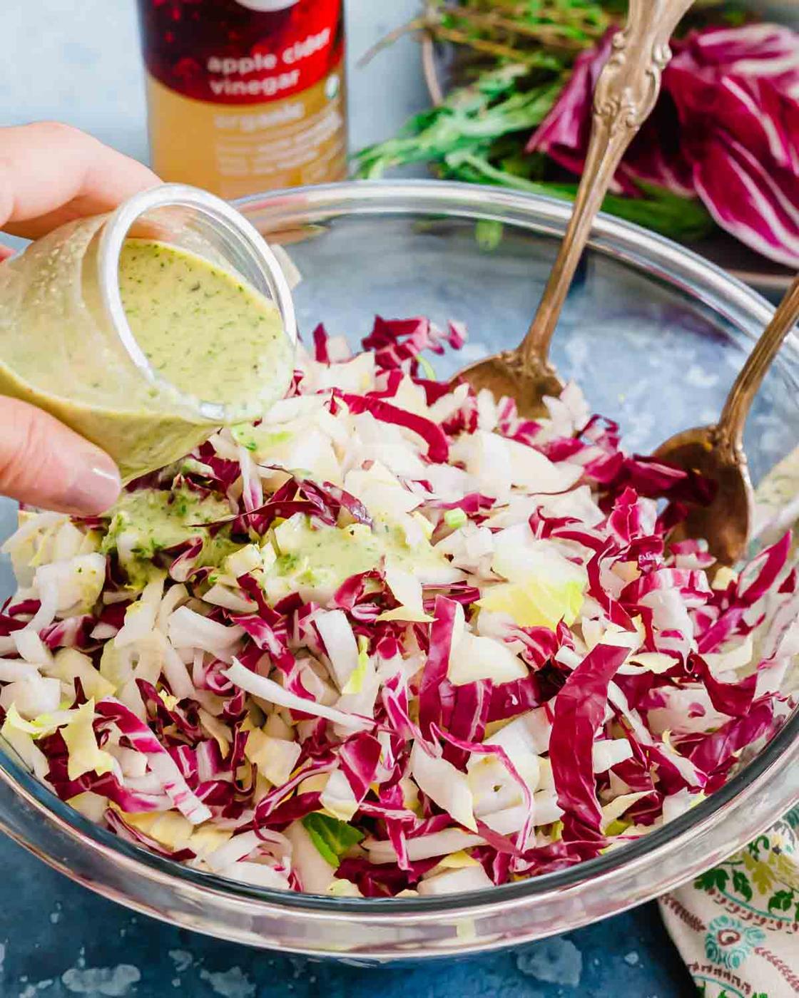 A person drizzling a dressing on an endive radicchio salad.