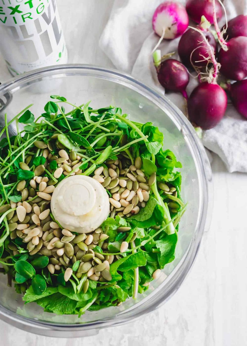 Radish greens in a food processor with ingredients to make pesto.