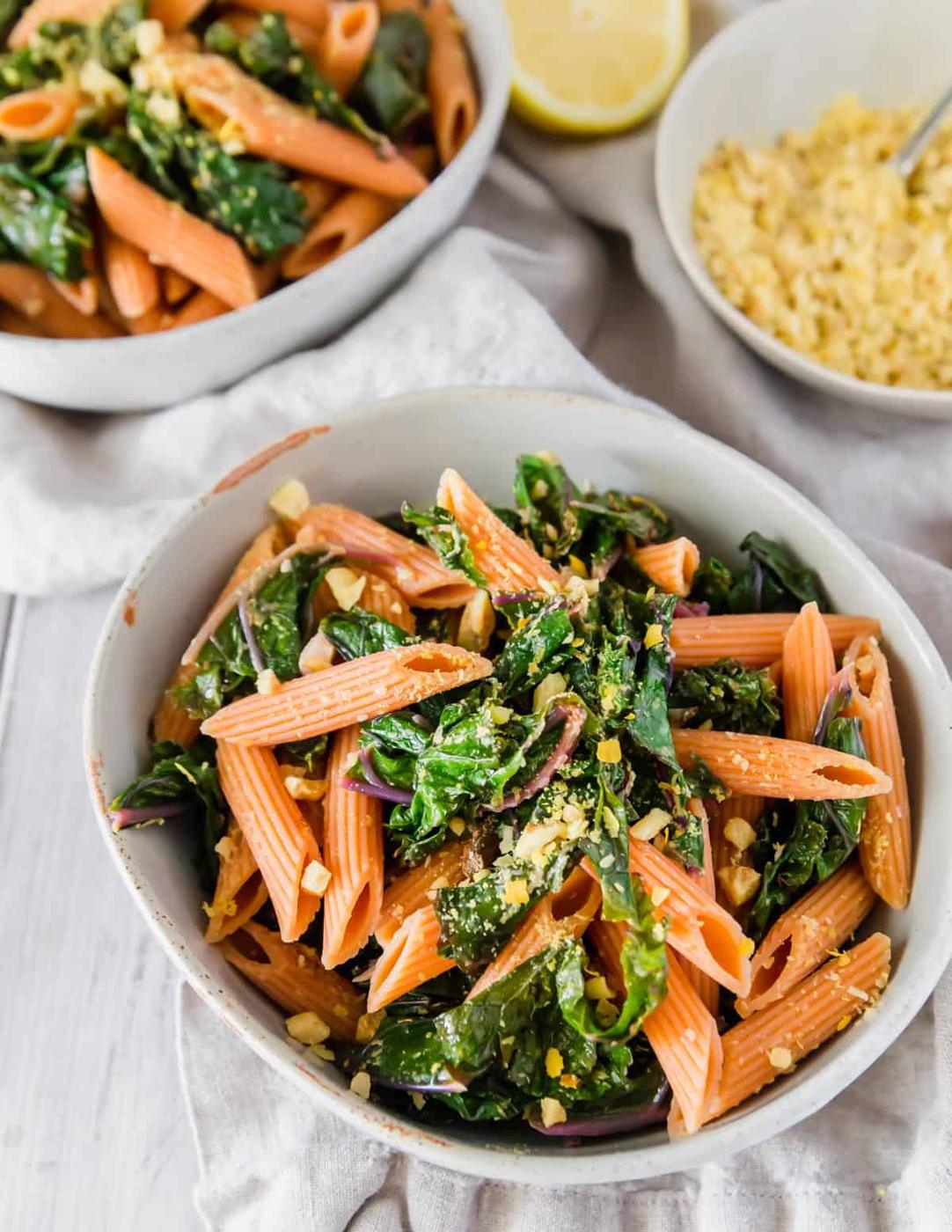 Gluten-free red lentil pasta is cooked then tossed with garlic lemon sautéed kale and topped with a walnut and nutritional yeast mixture for a delicious plant based vegan dinner.