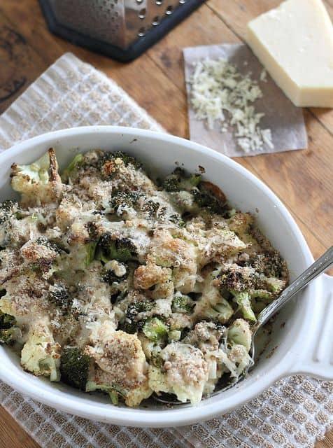 Roasted broccoli and cauliflower parmesan gratin in a large white serving bowl with a spoon.