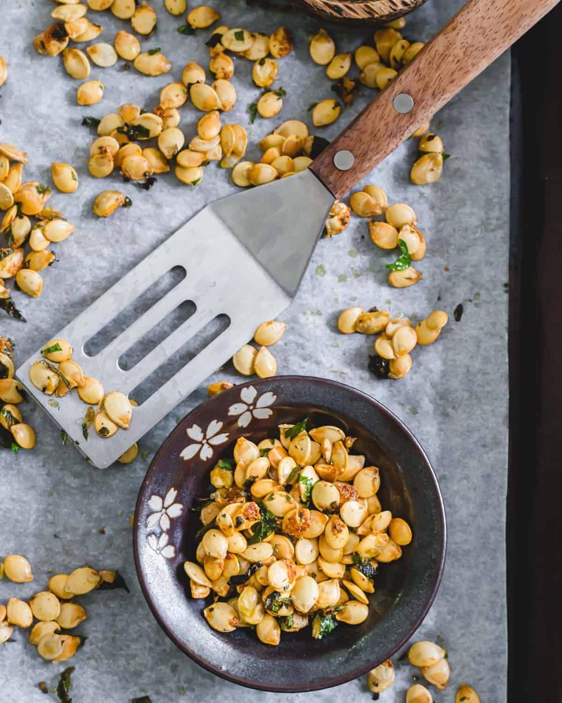 Roasted delicata squash seeds with garlic and herbs in a small bowl.