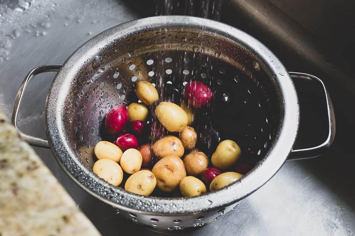 Rinsing baby potatoes under water in a colander.