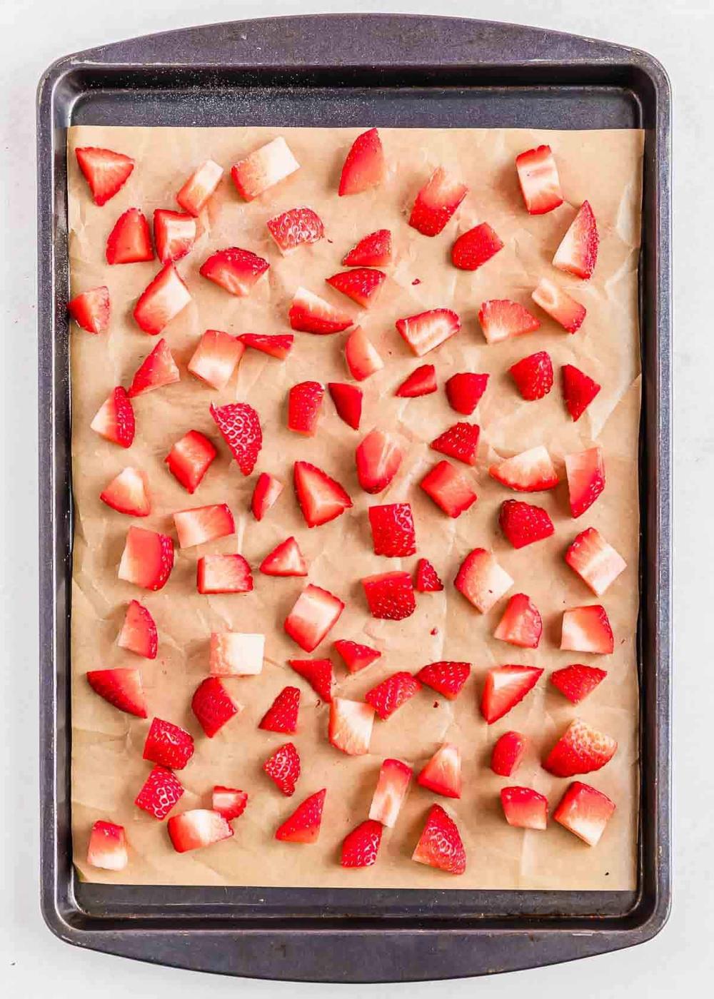 Cubed strawberries are spread evenly across a parchment-lined baking sheet.